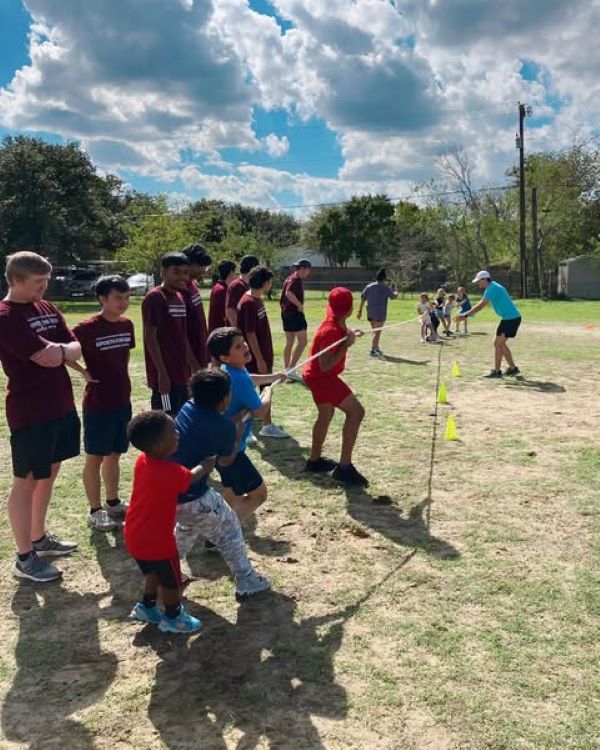 Group of college students watching kids play tug-of-war